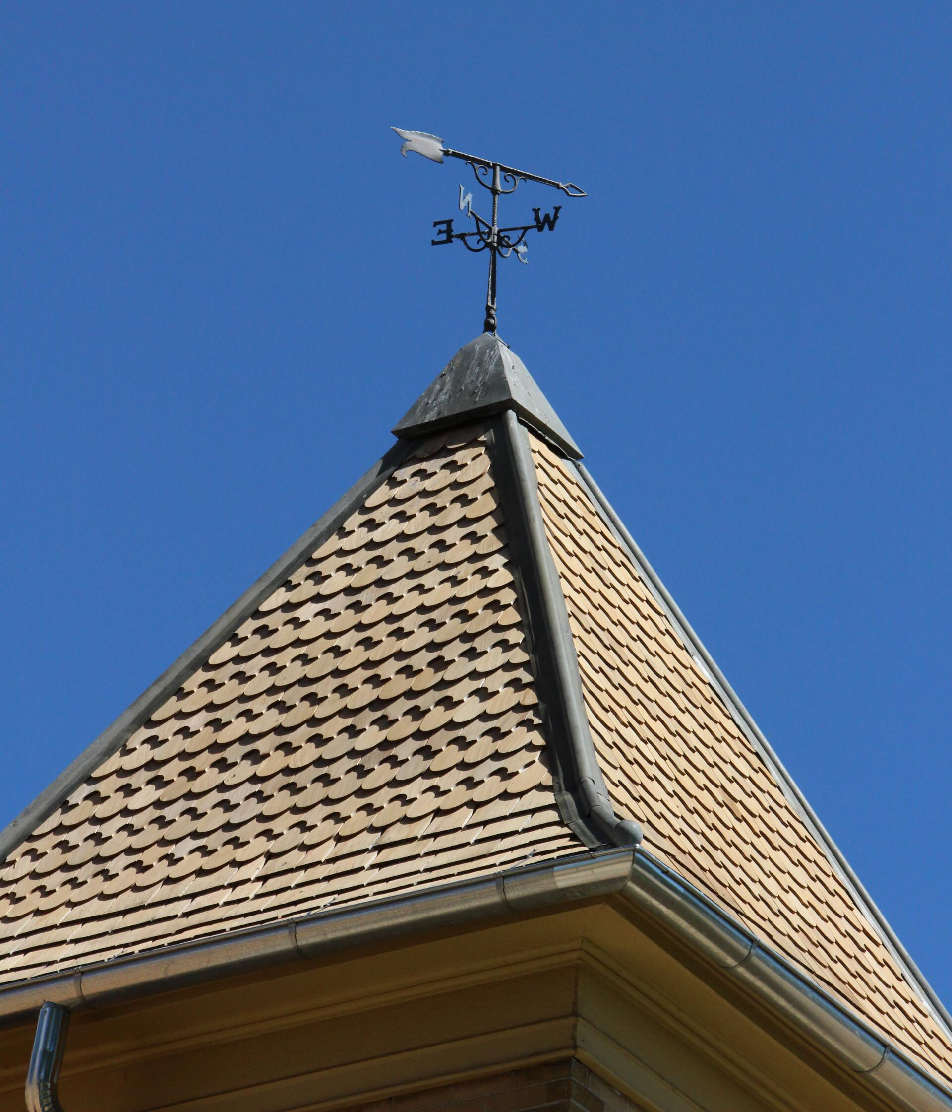 Steep shingled roof with a weather vane against a clear blue sky