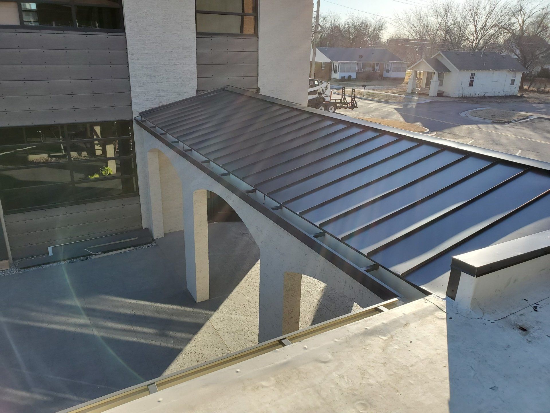 Modern metal roof over a covered walkway beside a building, with sunlight and a snowy street in the background