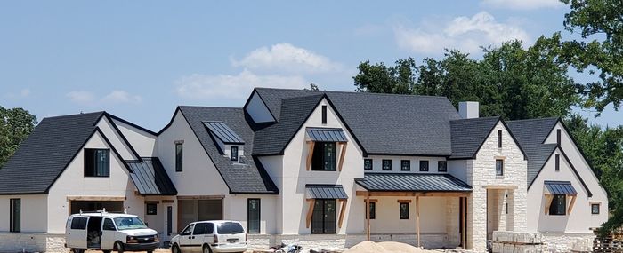Modern stone and gray-roof suburban house under construction with parked trucks and clear sky