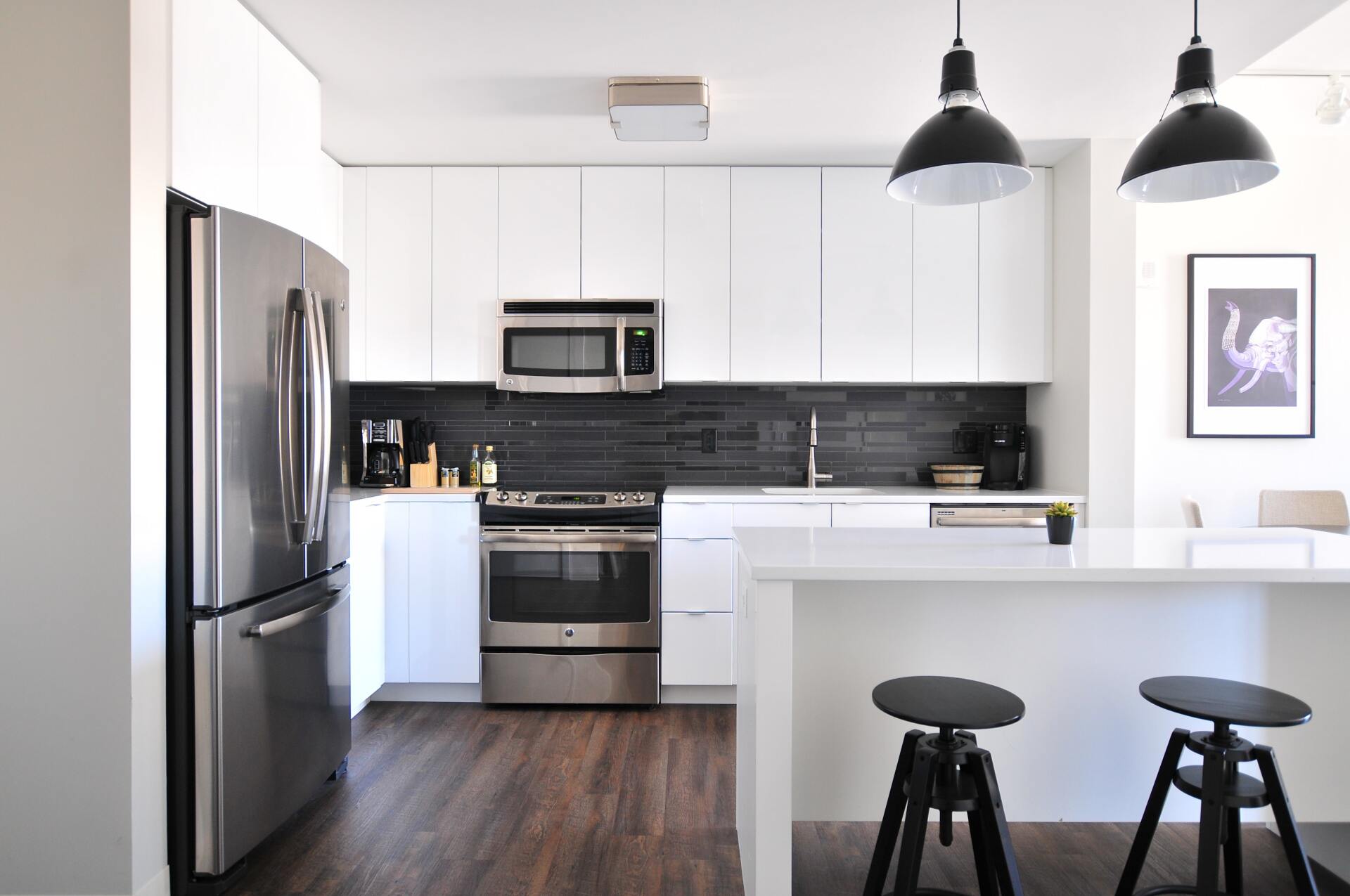 Modern kitchen with stainless steel appliances, white cabinets, black pendant lights, and a breakfast bar with stools