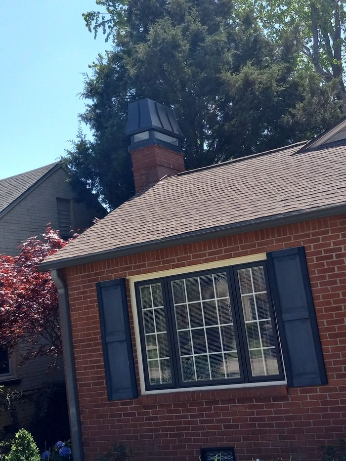 Brick house exterior with a tiled roof, window shutters, and a chimney under a clear blue sky