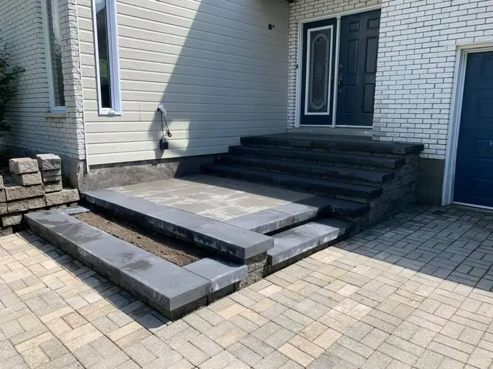 Plateforme en béton surélevée et marches menant à une porte d'entrée dans une cour pavée de briques