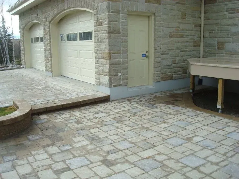 Maison en pierre avec deux portes de garage, une porte d'entrée latérale et une allée pavée.