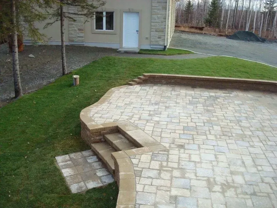 Terrasse en pierre à l'arrière de la maison, avec des marches courbes, jouxtant la pelouse.