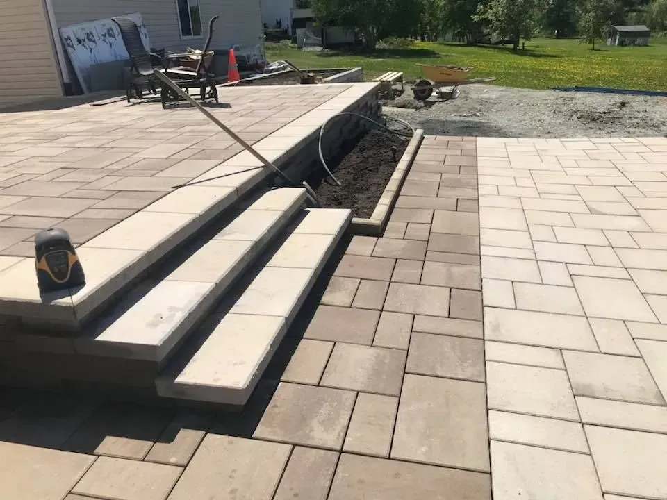 Terrasse avec marches à côté d'un fossé ouvert dans une cour arrière, avec une pelouse et des chaises en arrière-plan.