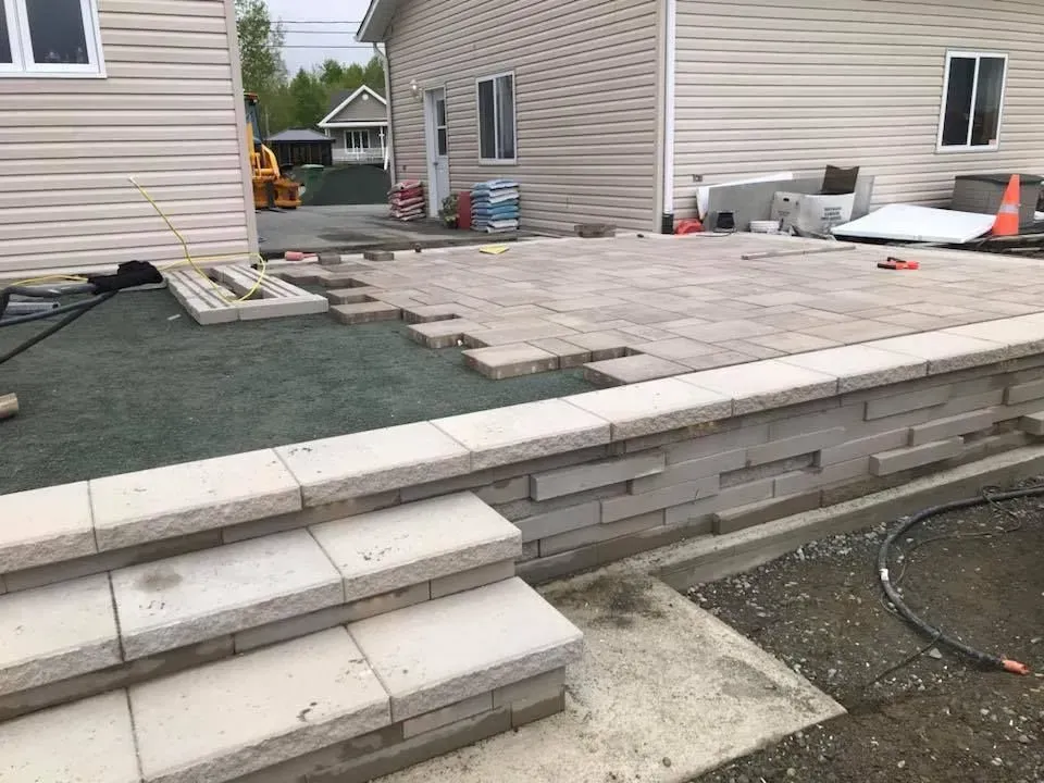 Terrasse arrière en construction avec pavés, marches et terrain non aménagé entre les maisons