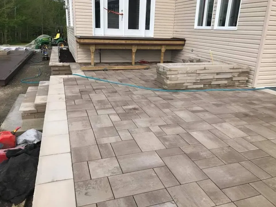 Terrasse arrière avec pavés gris, mur de soutènement et façade de maison en construction