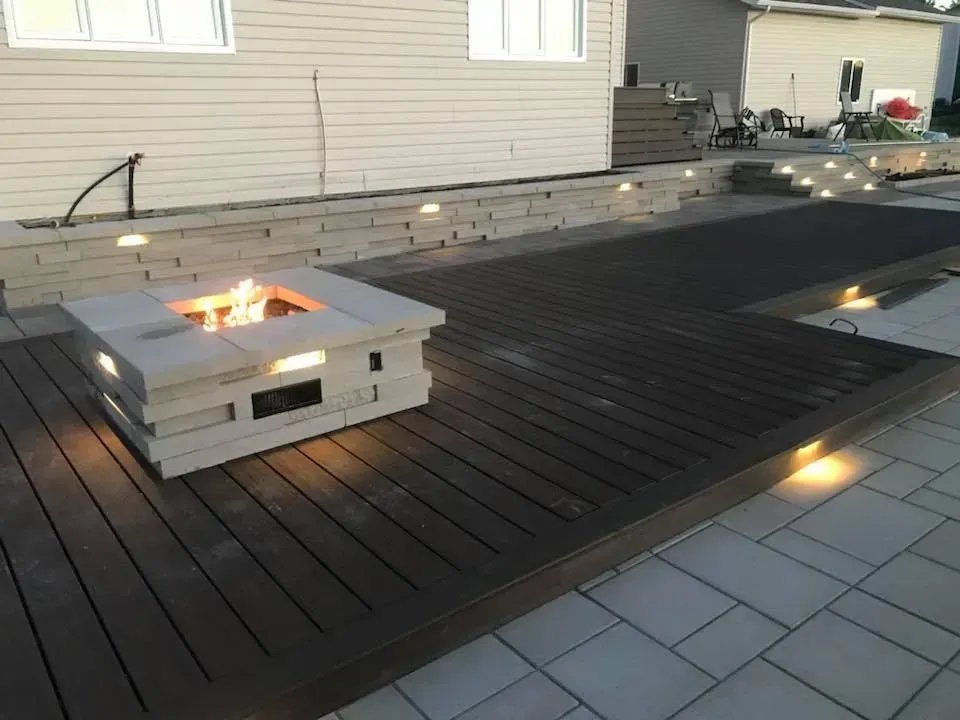 Patio moderne avec un foyer carré et une terrasse en bois foncé à côté d'une maison aux murs clairs
