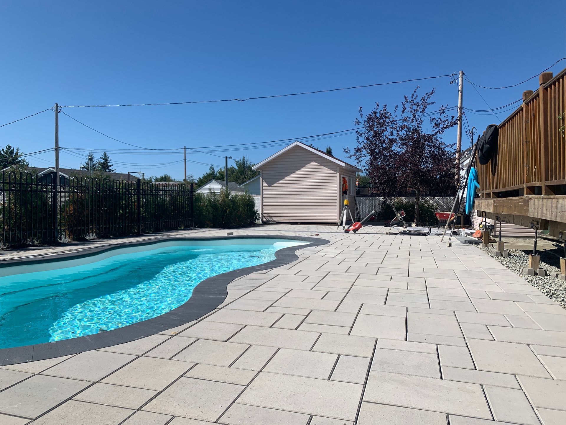 Piscine dans le jardin avec eau turquoise, terrasse en pierre et petit abri sous un ciel dégagé