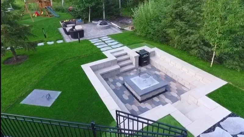 Terrasse arrière avec un foyer moderne, un coin salon en pierre et une pelouse verdoyante et arborée.
