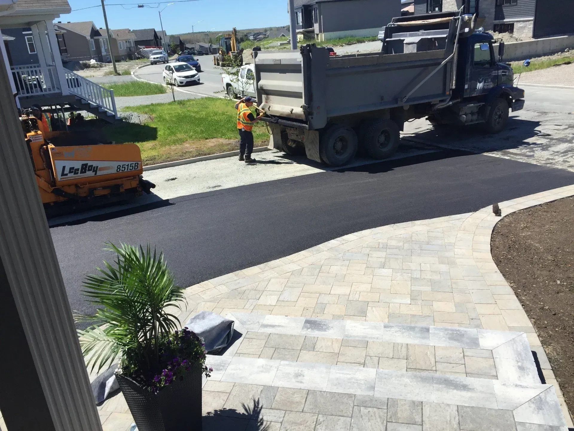 Une équipe de travaux publics effectue le pavage d'une rue résidentielle à côté d'un trottoir et d'un camion utilitaire stationné.