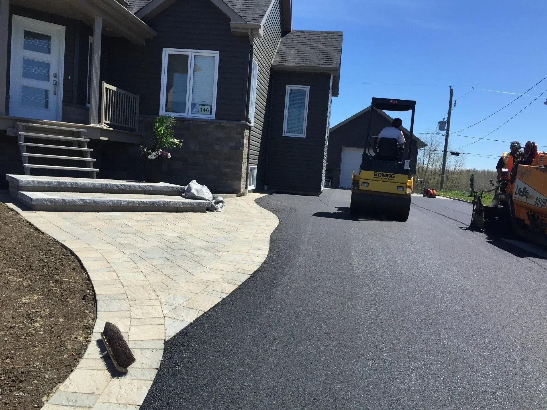 Travaux de pavage le long d'une maison en pierre avec un nouveau trottoir incurvé et des engins de chantier à proximité