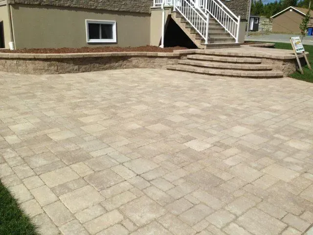 Terrasse pavée et marches jouxtant une maison avec une petite fenêtre et une balustrade blanche.
