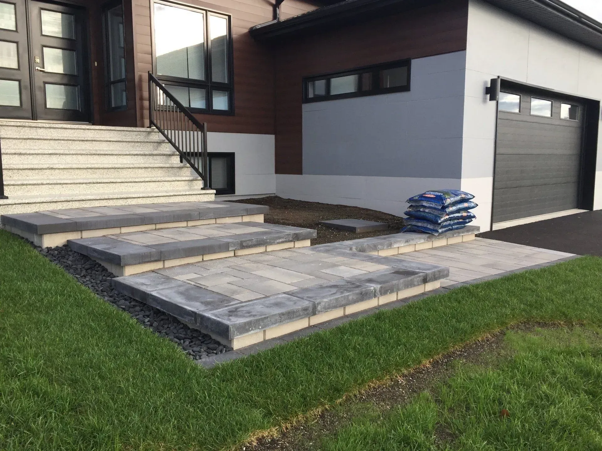 Entrée de maison moderne avec marches de patio en pierre, porte de garage et un tas de pavés sur la droite