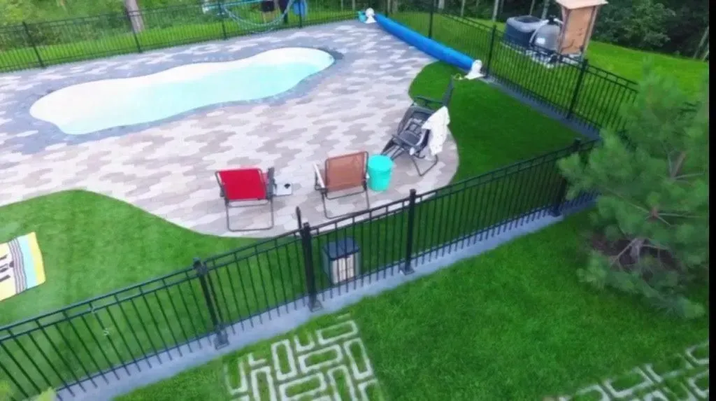 Espace piscine dans le jardin avec chaises longues, table, chaises rouges et turquoise et clôture noire
