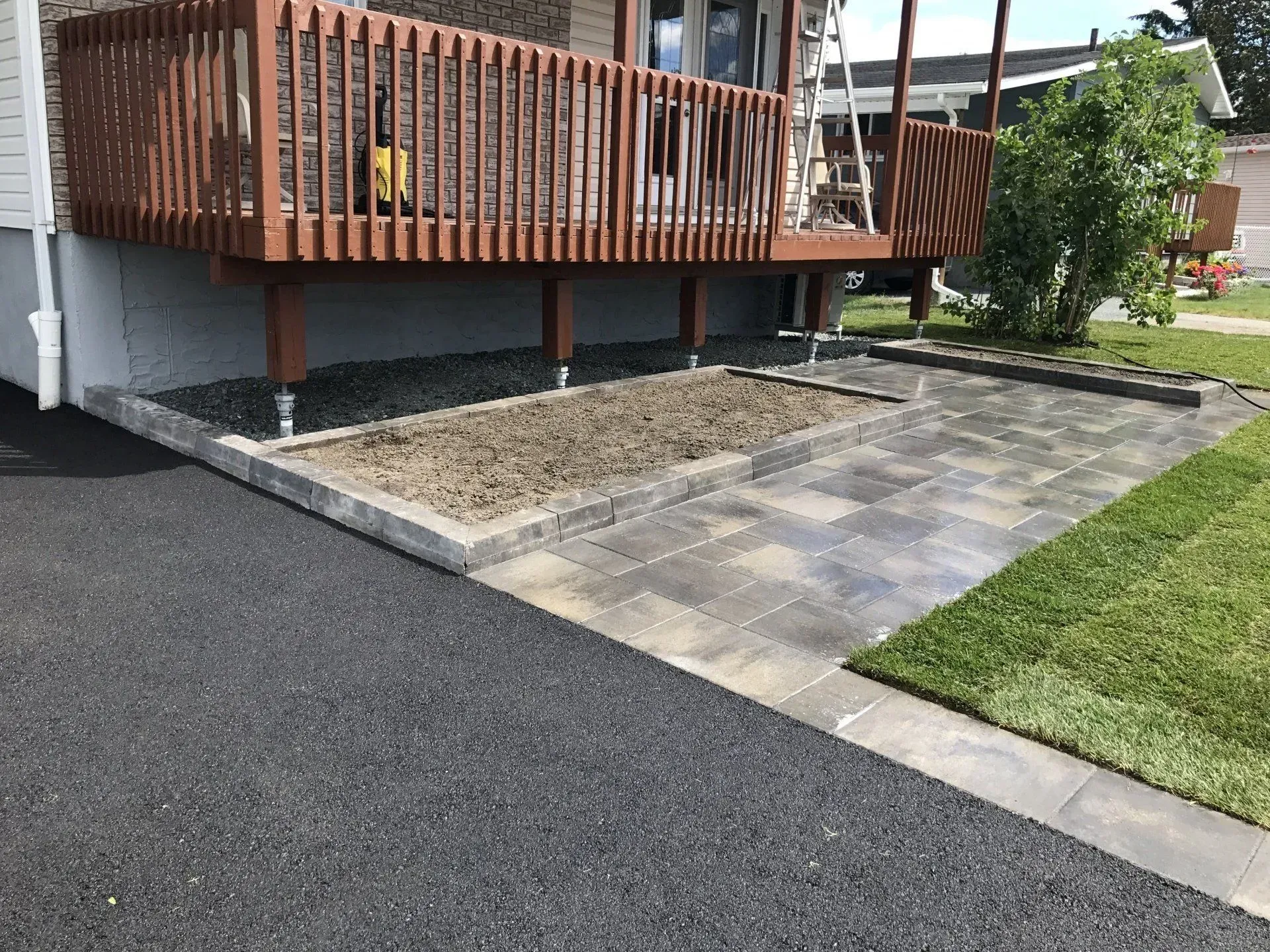 Véranda avec rambarde en bois, terrasse pavée, allée de gravier et petit jardin.