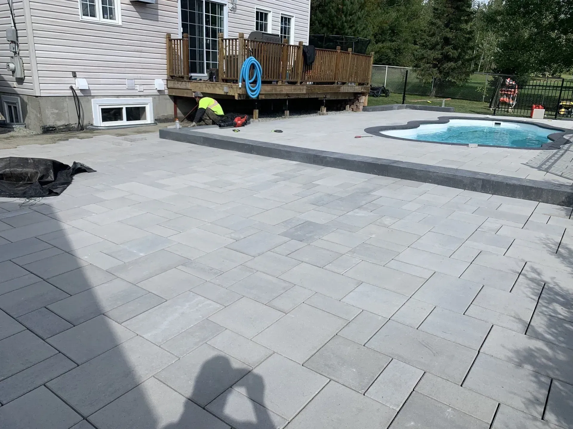 Terrasse arrière avec pavés gris, petite piscine, terrasse en bois et façade de maison en pierre.