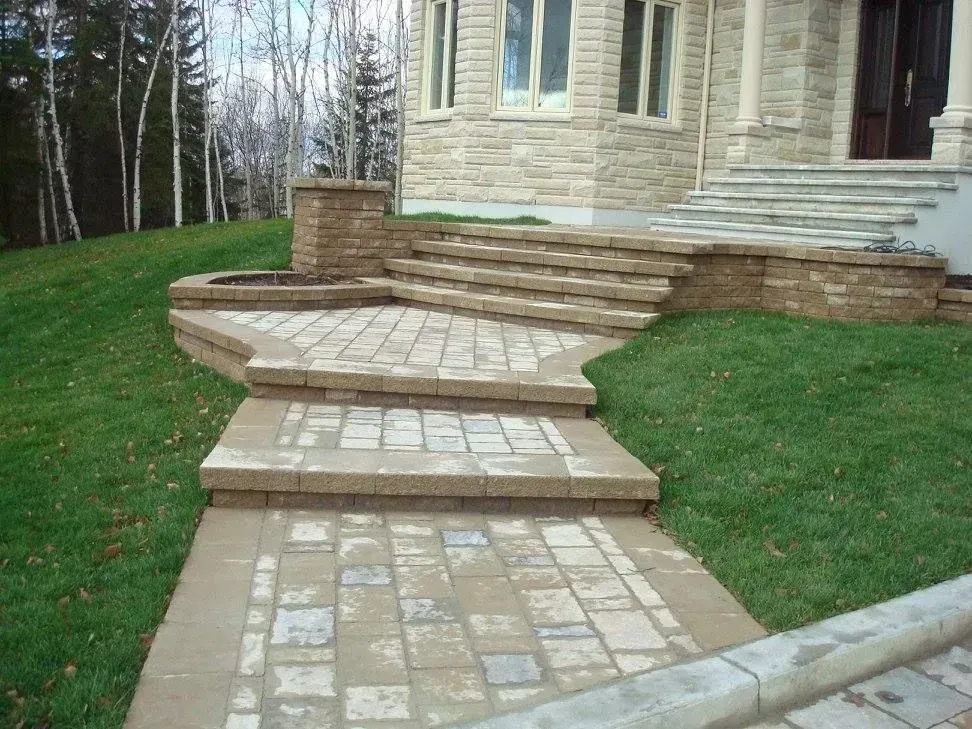 Allée et marches en pierre menant à l'entrée d'une maison, de l'autre côté d'une pelouse verte, avec des arbres en arrière-plan.