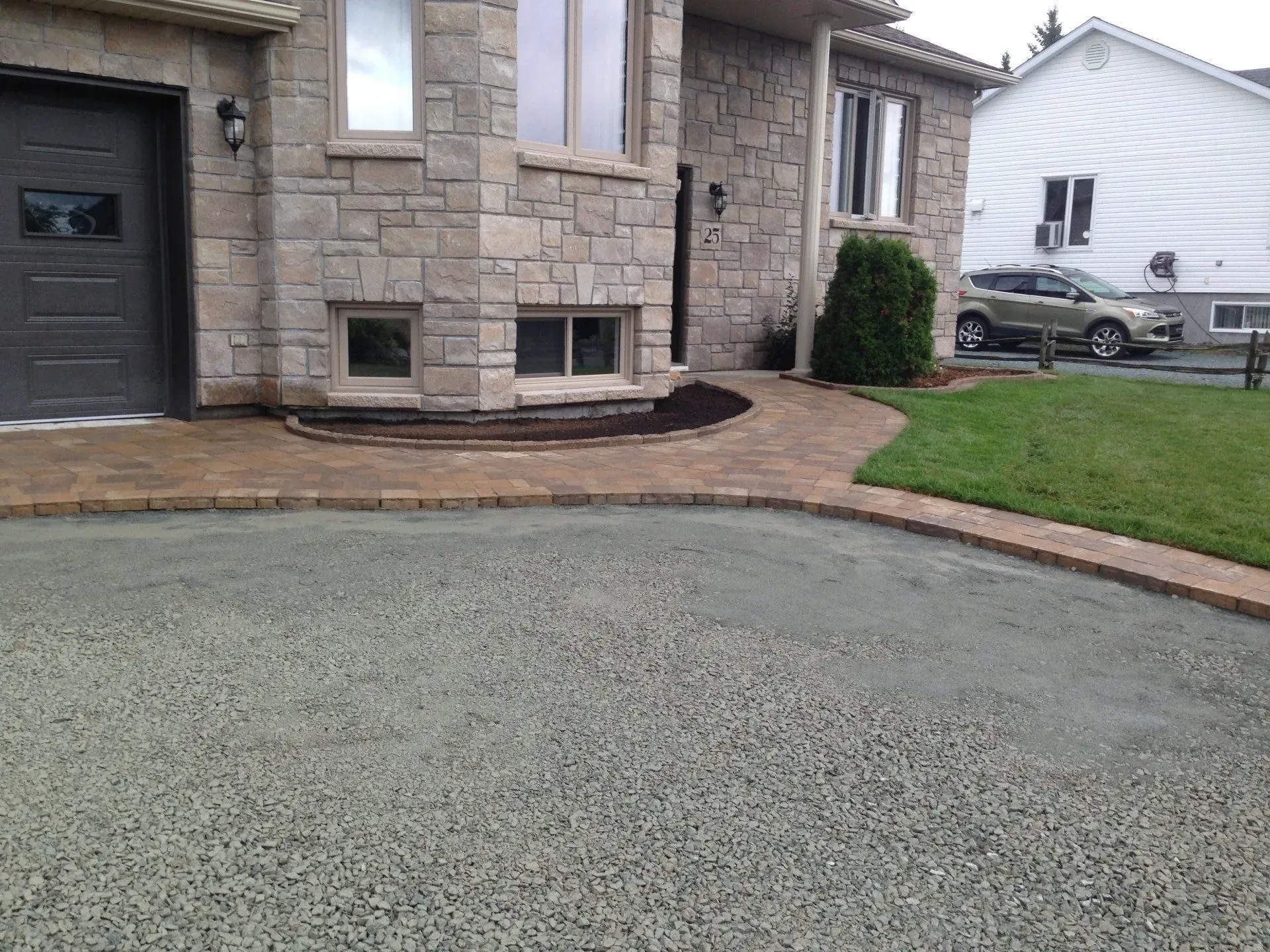 Entrée de maison en pierre avec porte de garage noire, allée en briques et allée de gravier.
