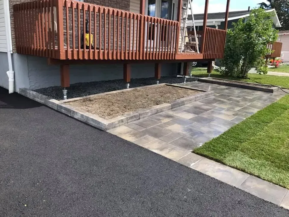 Terrasse en bois surélevée jouxtant un patio pavé et une pelouse, avec un petit parterre de fleurs en dessous.