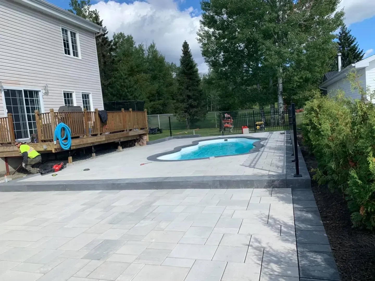 Terrasse arrière avec piscine creusée, terrasse en bois et arbres sous un ciel nuageux