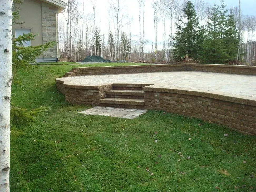 Terrasse arrière avec muret en pierre, marches et pelouse à côté d'une maison et d'arbres
