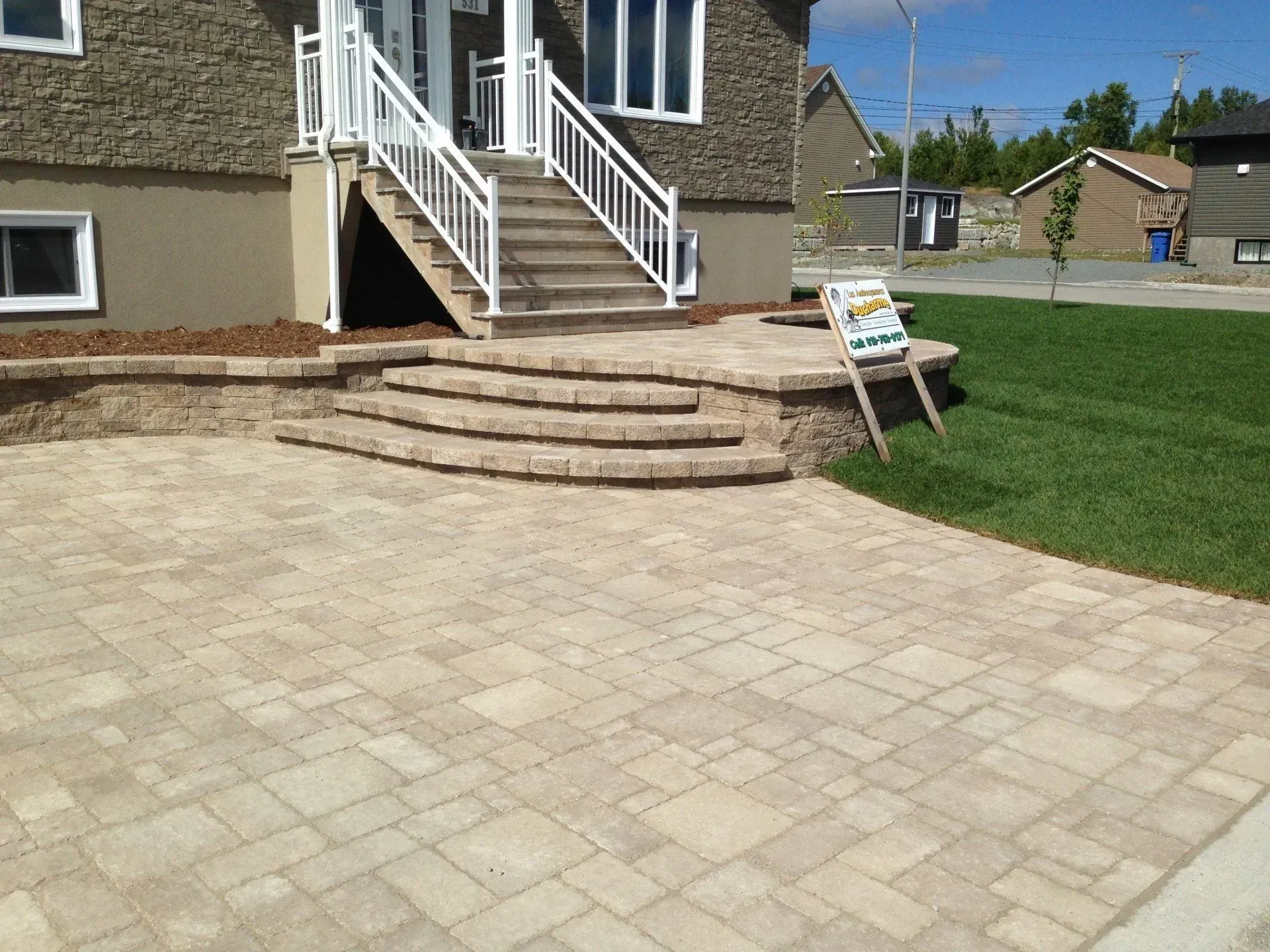 Terrasse pavée avec des marches en pierre incurvées menant à l'entrée de la maison et à une pelouse à côté d'un petit panneau.