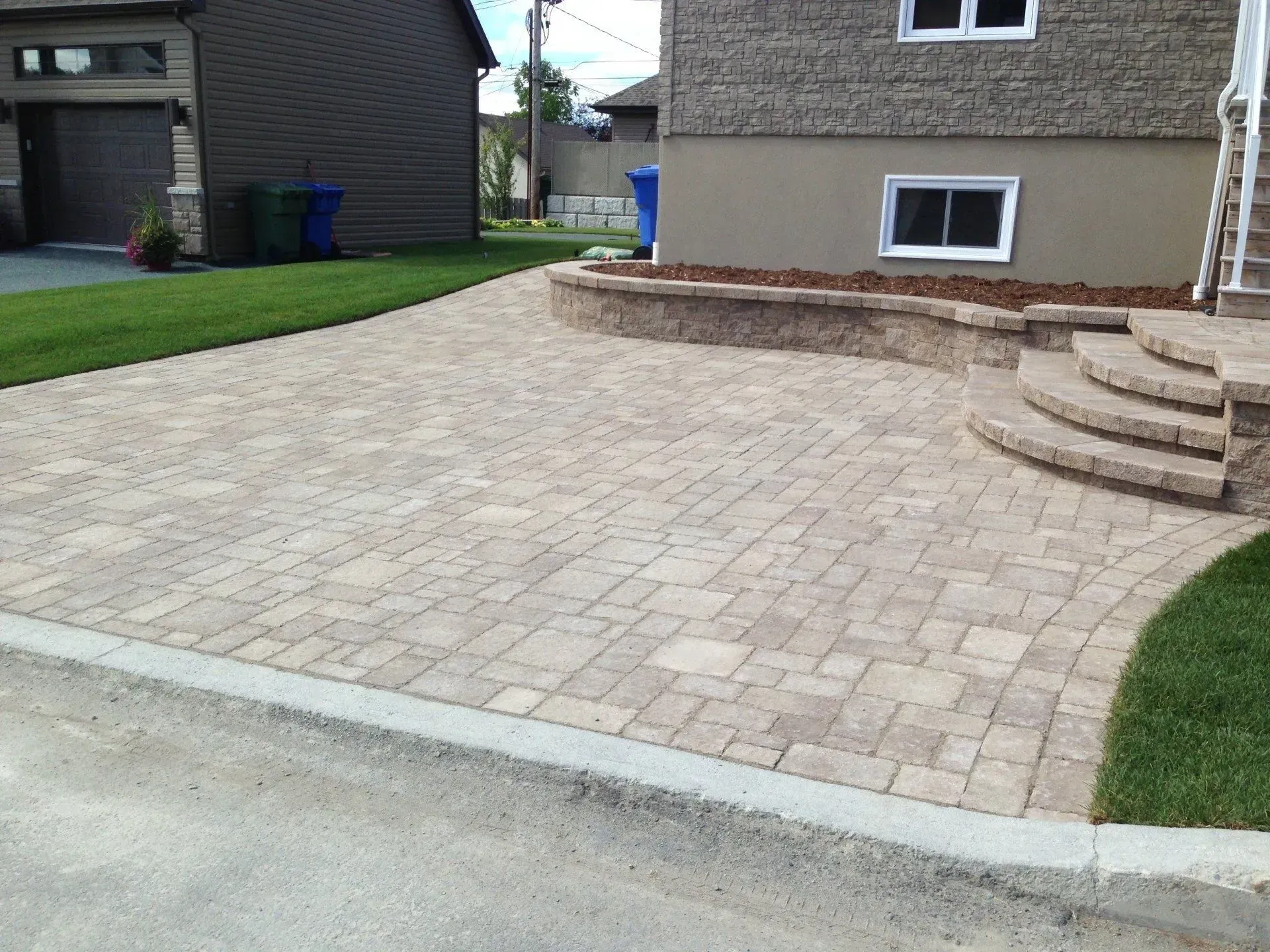 Allée résidentielle avec terrasse en pavés beiges, marches en pierre et pelouses adjacentes.