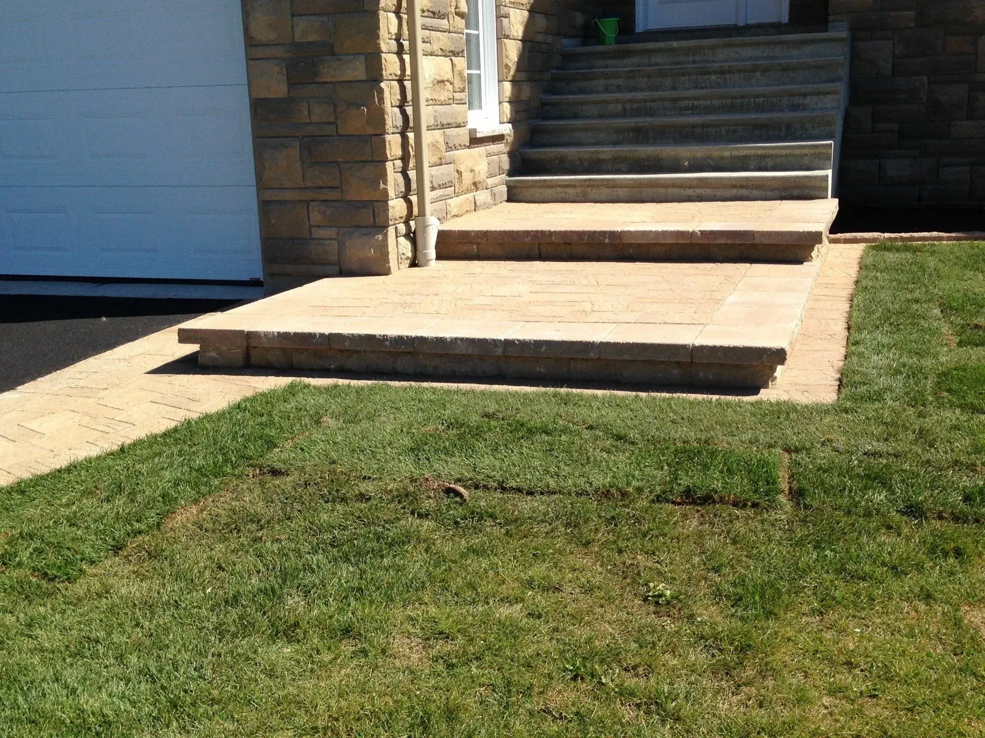 Des marches et une rampe en béton mènent à une porte d'entrée située à côté d'un garage, avec une pelouse.