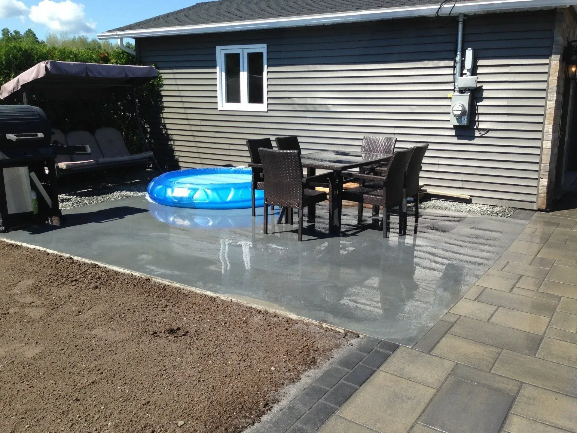 Terrasse arrière avec ensemble de salle à manger extérieure, pataugeoire bleue et pelouse à côté d'une maison