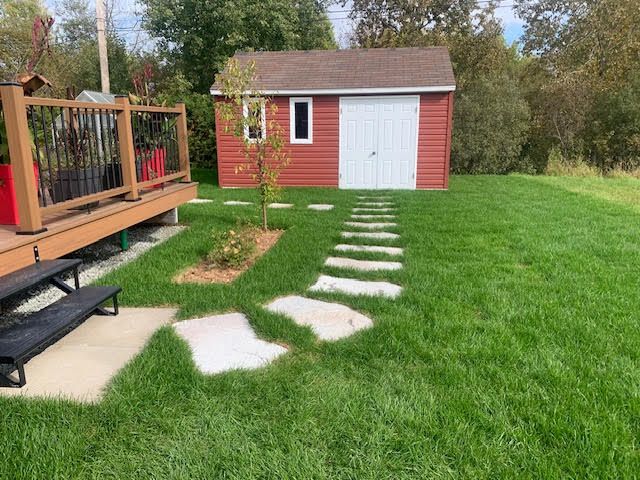 Jardin avec des pas japonais traversant une pelouse verte menant à un abri de jardin rouge à côté d'une terrasse en bois.