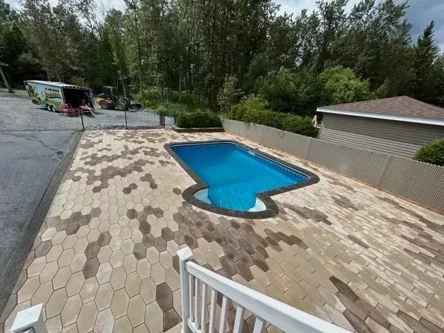 Terrasse arrière avec piscine bleue, dalles beiges et arbres en arrière-plan