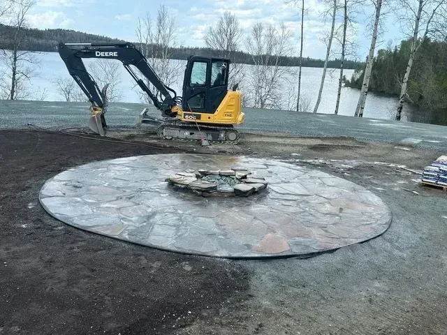 Une excavatrice sur un chantier de construction au bord d'un lac, à côté d'une grande dalle circulaire en béton.