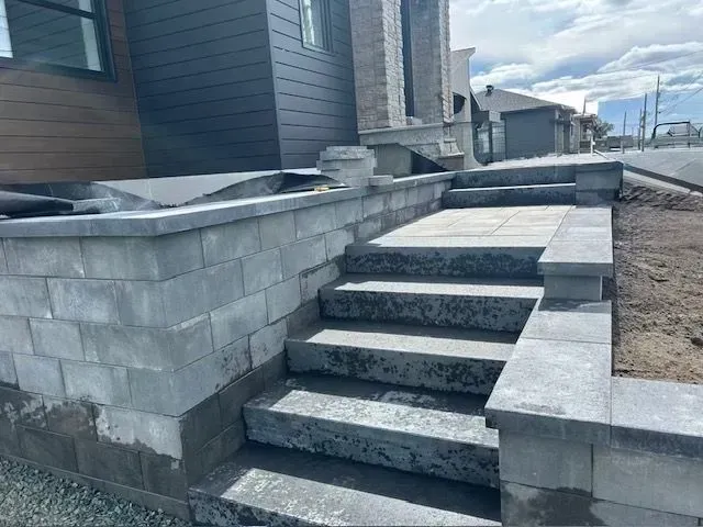 Des marches en béton mènent à l'entrée d'une maison bordée de murs de soutènement en pierre grise et de gravier.