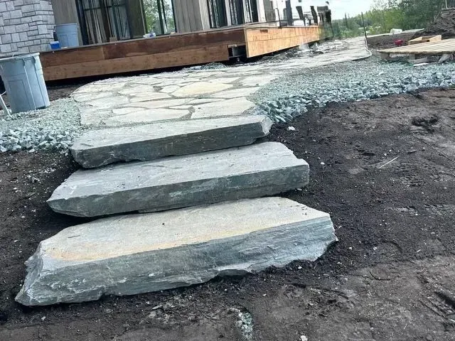 Des marches en pierre mènent à une terrasse en bois dans une cour en gravier et en terre.