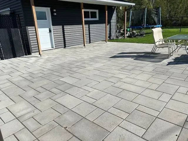 Terrasse pavée attenante à une maison, avec chaises d'extérieur et petite table ensoleillée.