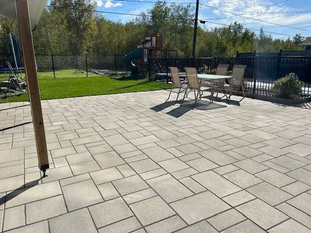 Terrasse avec dalles de pierre claire, table et chaises de jardin, cour clôturée et aire de jeux extérieure sous un ciel ensoleillé