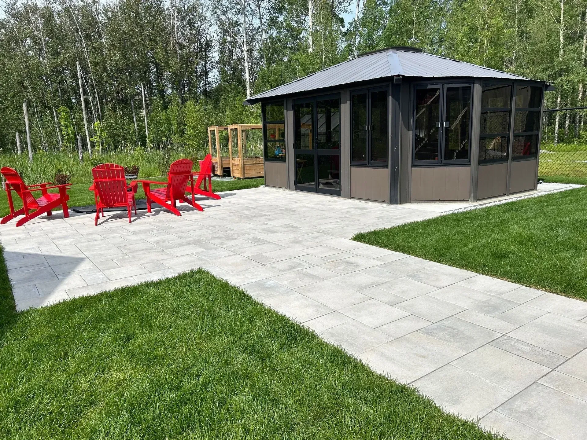 Terrasse avec chaises rouges et petite tonnelle couverte à côté d'une pelouse et d'arbres