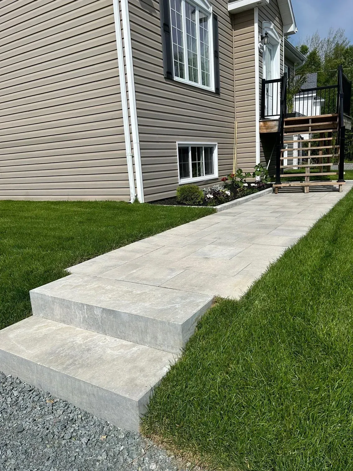 Allée en béton avec une petite marche menant à une maison beige et une pelouse verte