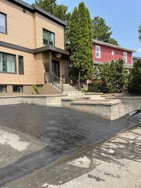 Entrée d'un immeuble résidentiel avec marches en béton, allée sombre et arbres bordant des maisons beiges et rouges