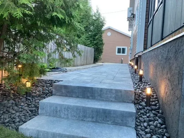 Des marches en pierre mènent à un chemin paysager latéral longeant une maison au crépuscule.
