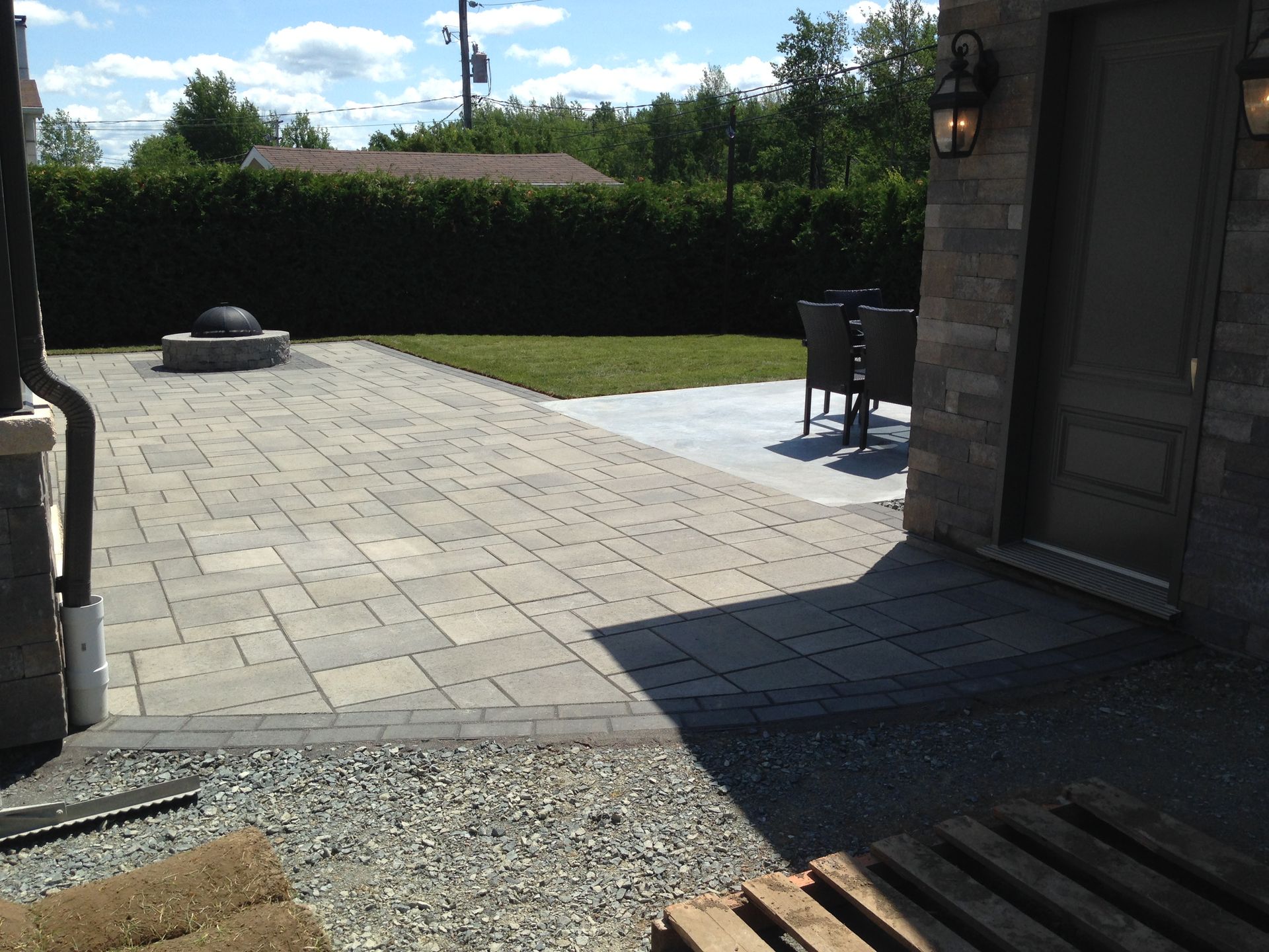 Terrasse avec dalles de pierre claire, bordure de gravier, haie et muret partiel baigné de soleil