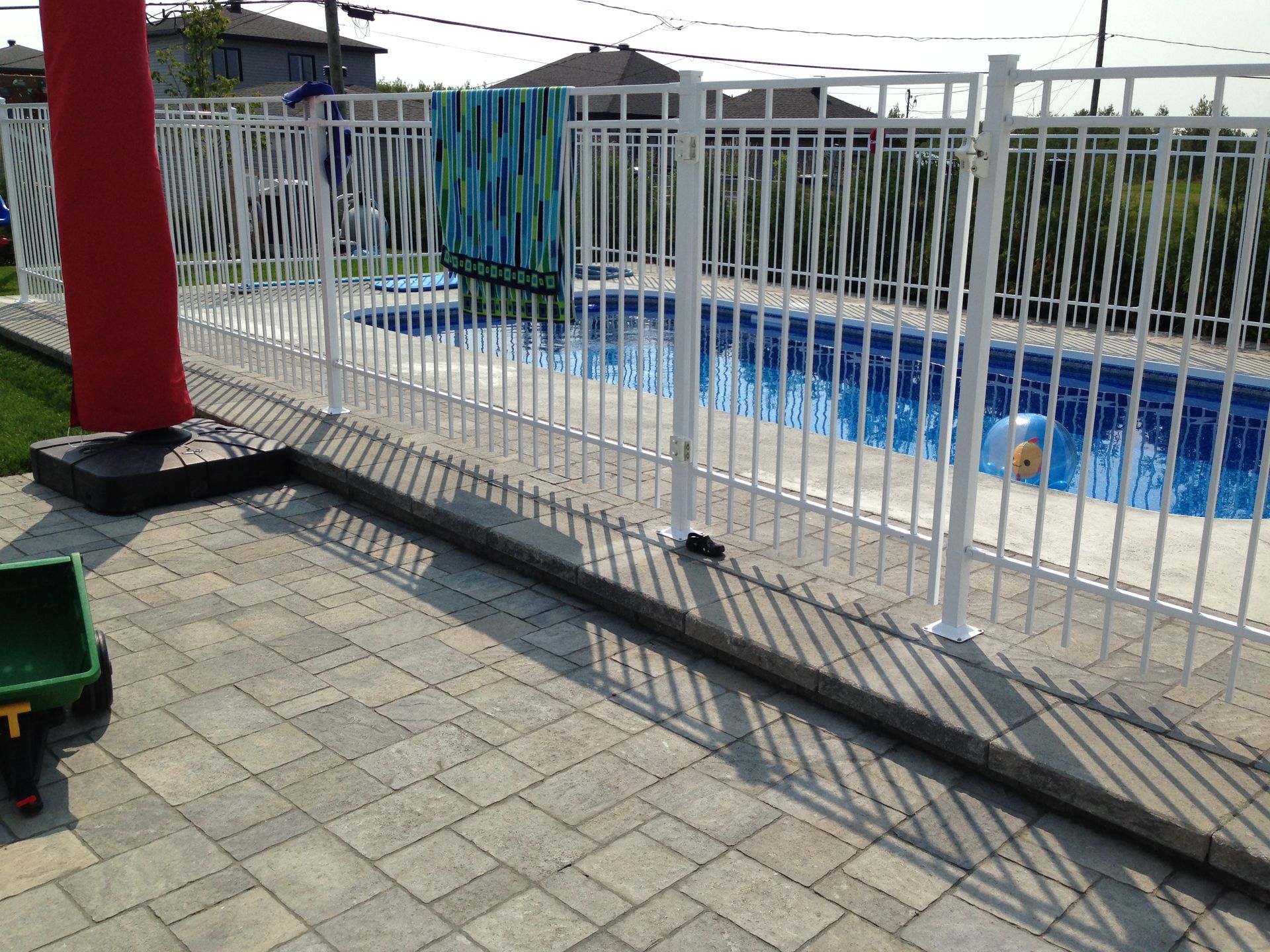 Clôture blanche à côté d'une piscine bleue sur une terrasse carrelée, avec un poteau rouge et une serviette suspendue à proximité.