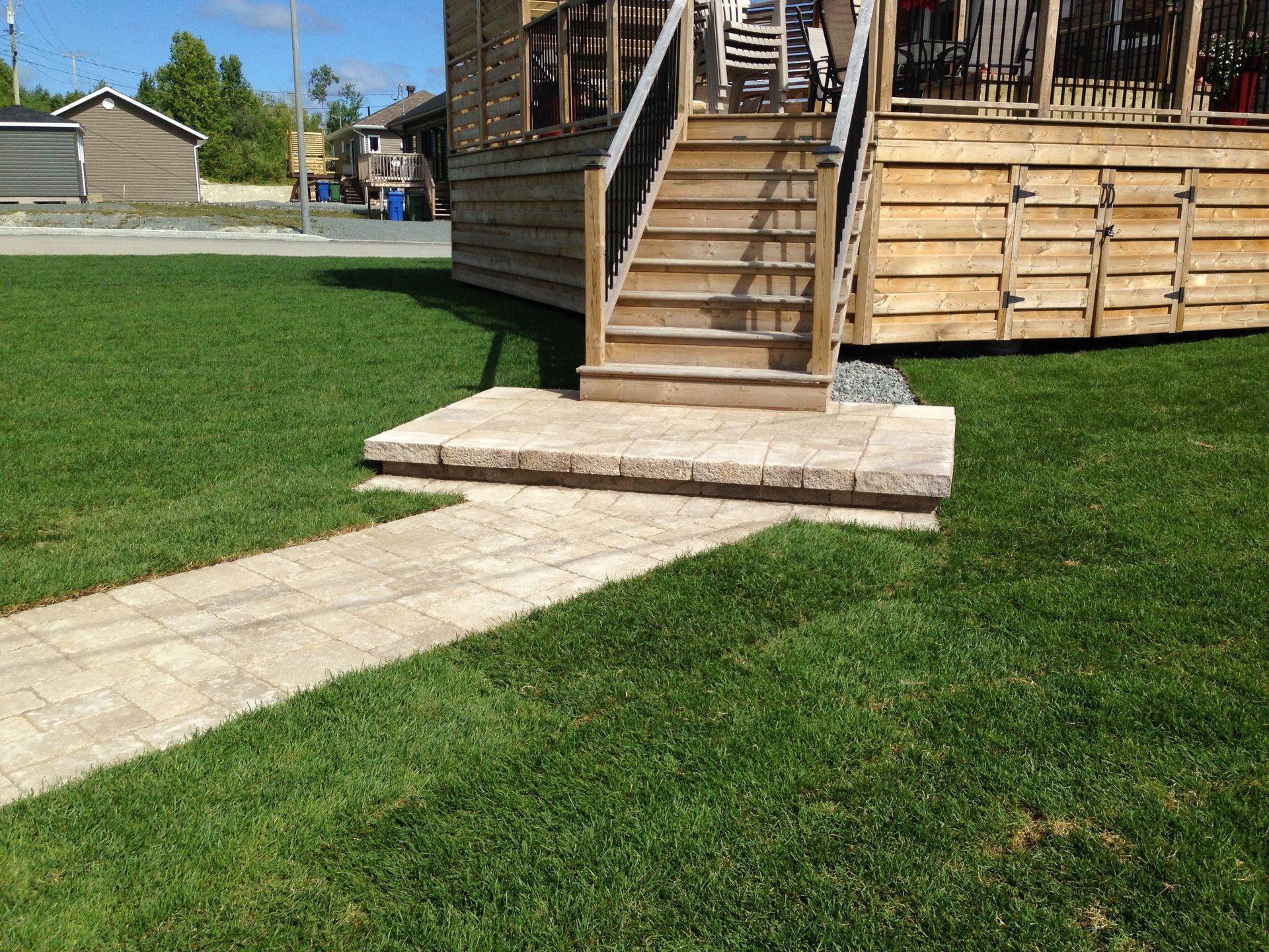 Escalier en bois menant à une terrasse et allée en béton traversant une pelouse verte