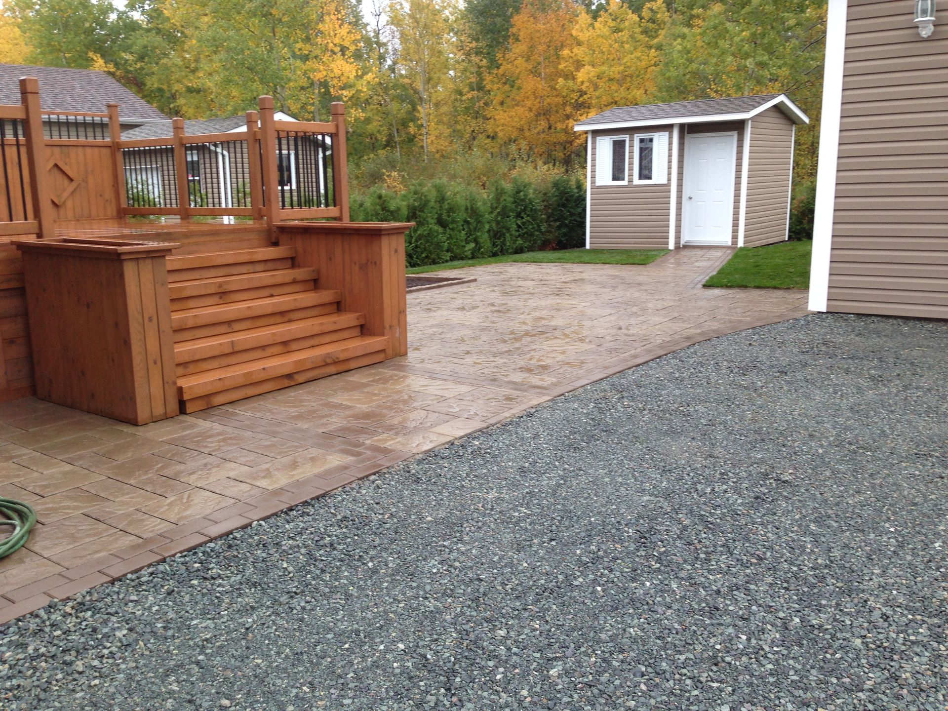 Terrasse arrière avec escalier en bois, allée de gravier et petit abri de jardin à côté de la maison
