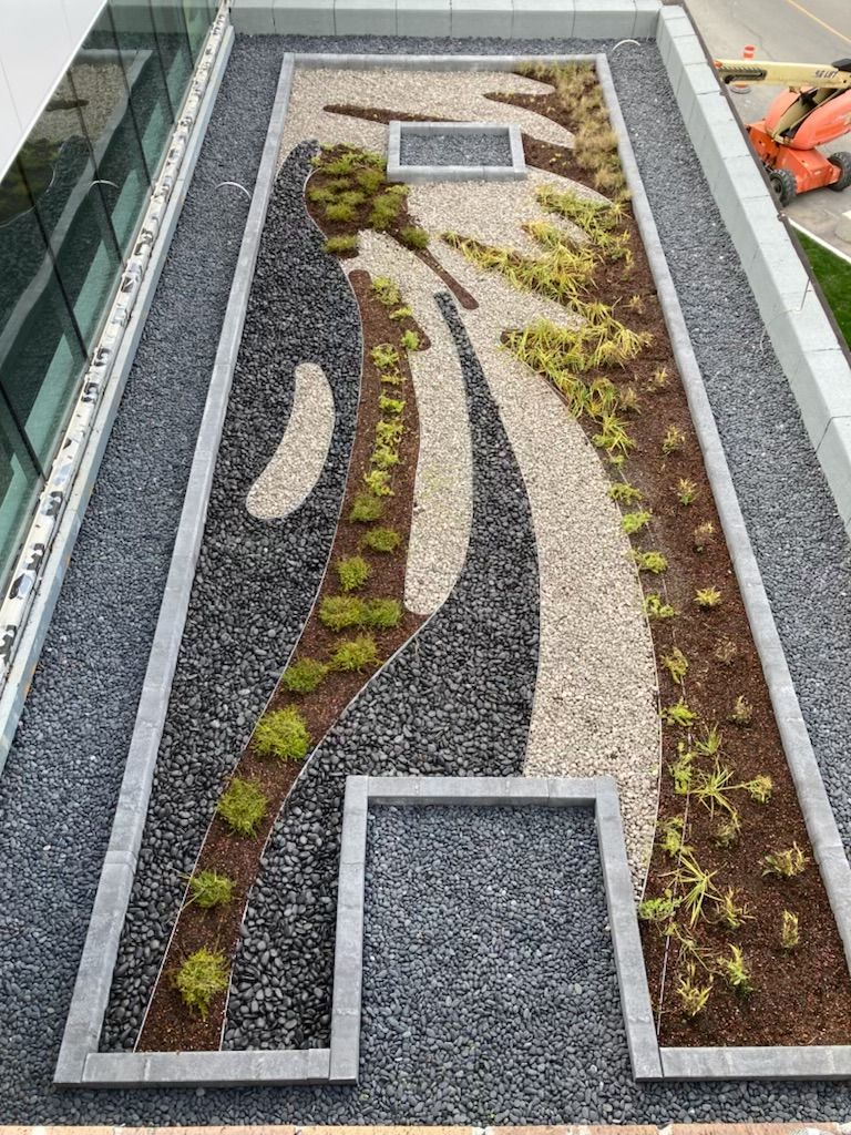 Un jardin décoratif sur le toit, avec des allées de gravier, des bordures en pierre et des plantes vertes basses.