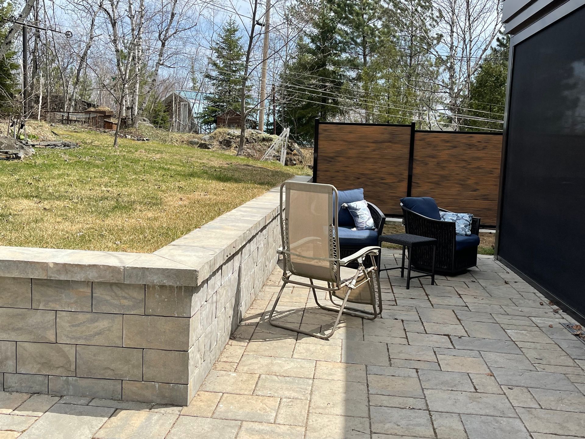 Terrasse avec deux chaises et une petite table le long d'un muret de jardin en pierre surélevé, donnant sur une cour gazonnée.