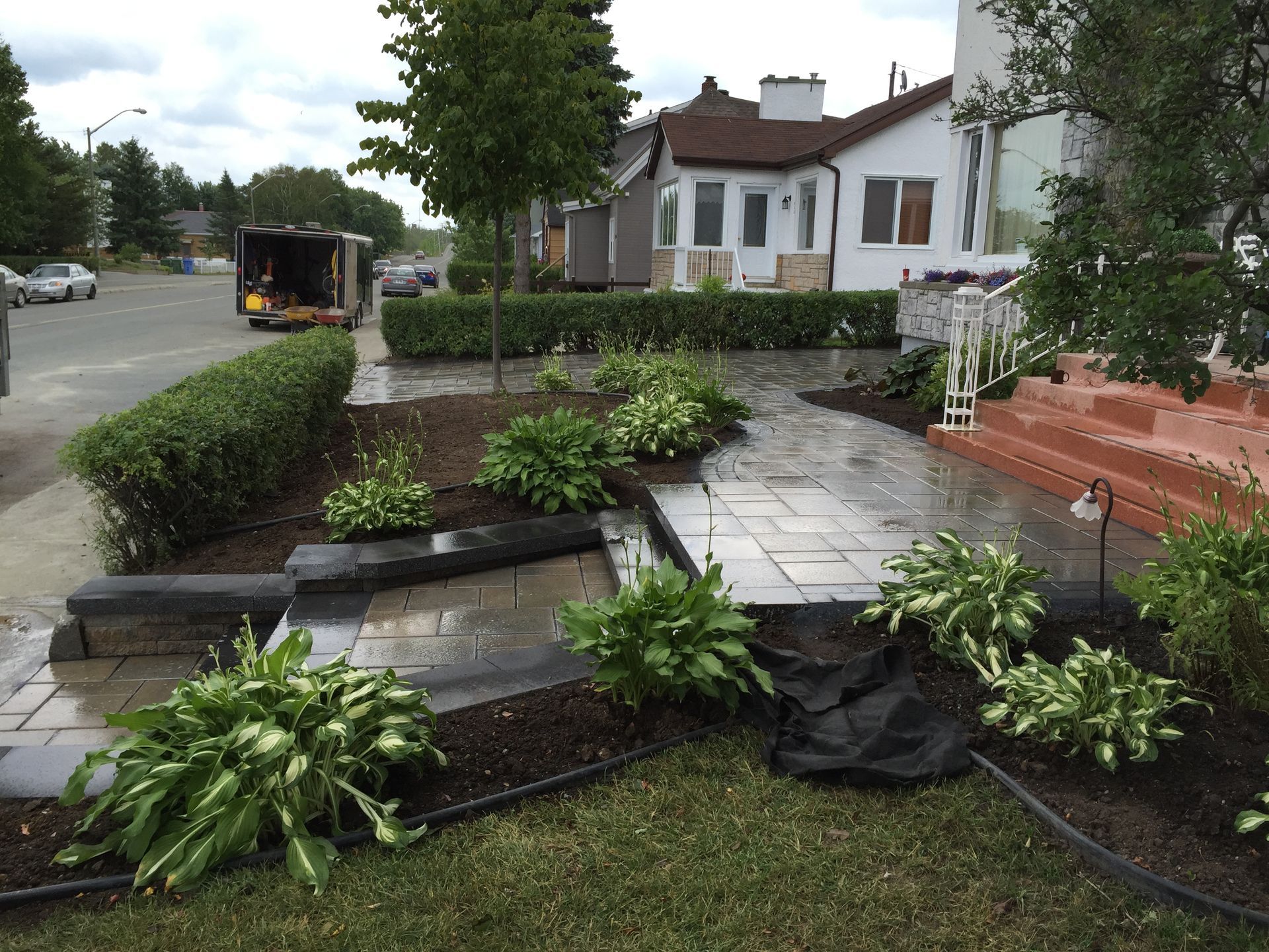 Jardin de devant avec marches en pierre, parterres de fleurs et maisons blanches le long d'une rue