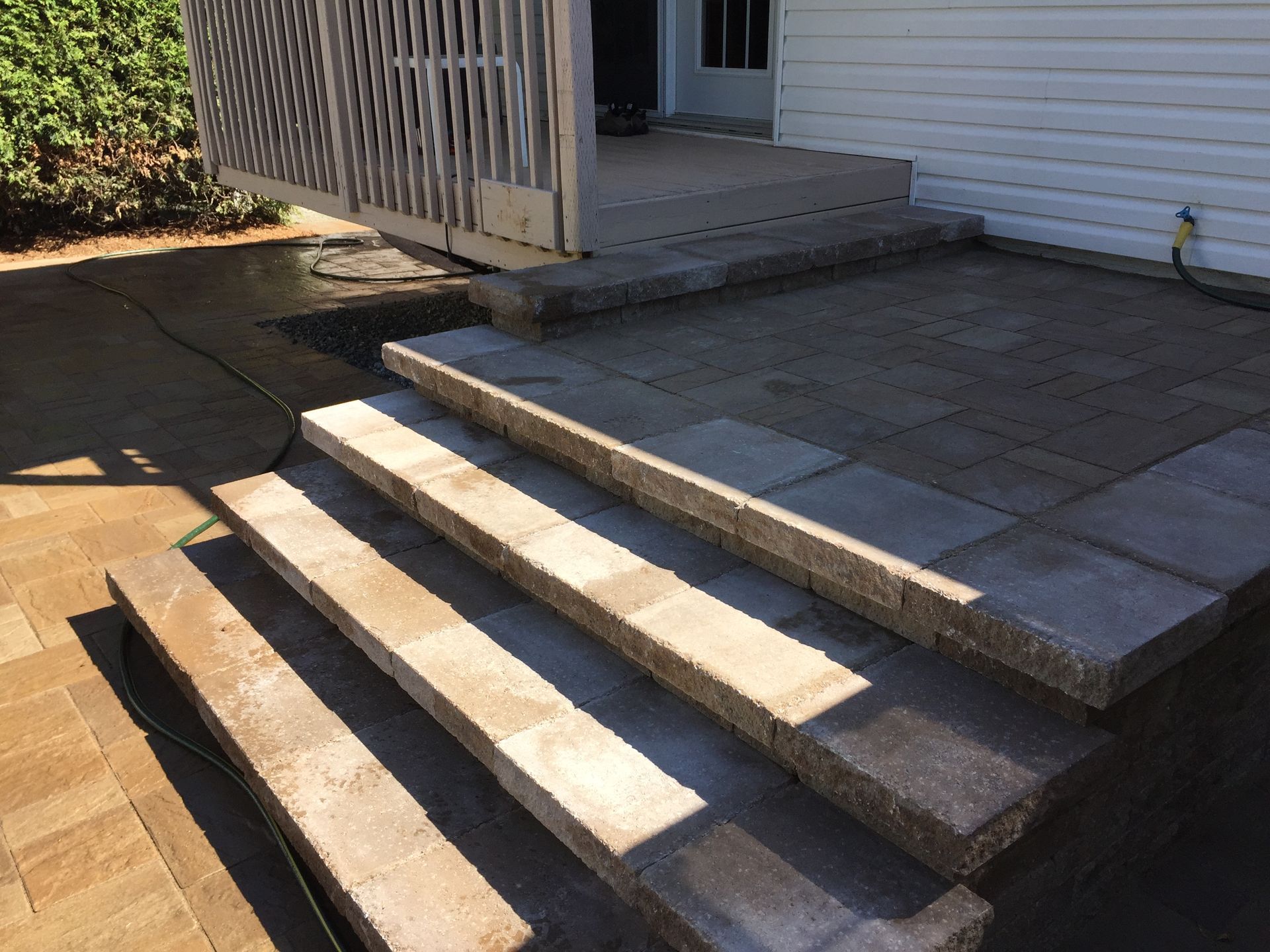Des marches en pierre mènent à une terrasse surélevée jouxtant une maison blanche et une balustrade en bois.