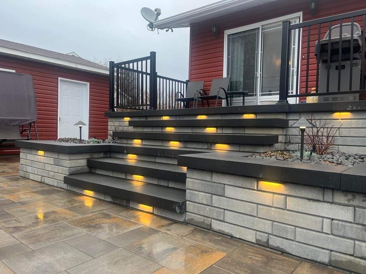 Patio moderne en briques avec marches en pierre éclairées menant à une petite terrasse et des portes vitrées
